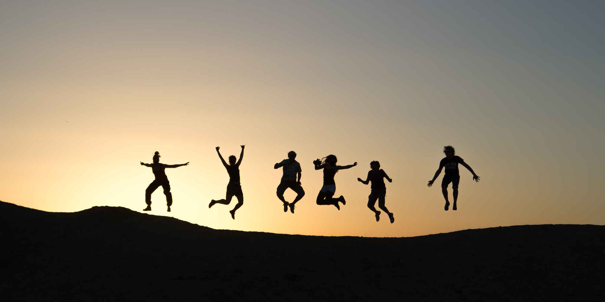 group of people jumping in the air with the sunset 