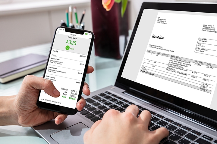 Person viewing invoice on smartphone and laptop