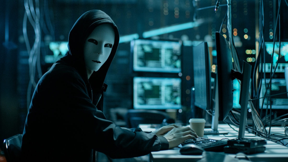man wearing a creepy mask in front of his computer
