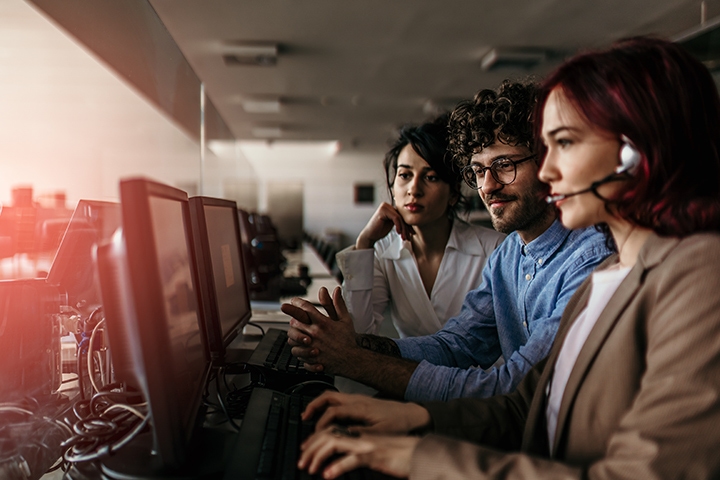 three customer support operators working in front of a row of computers