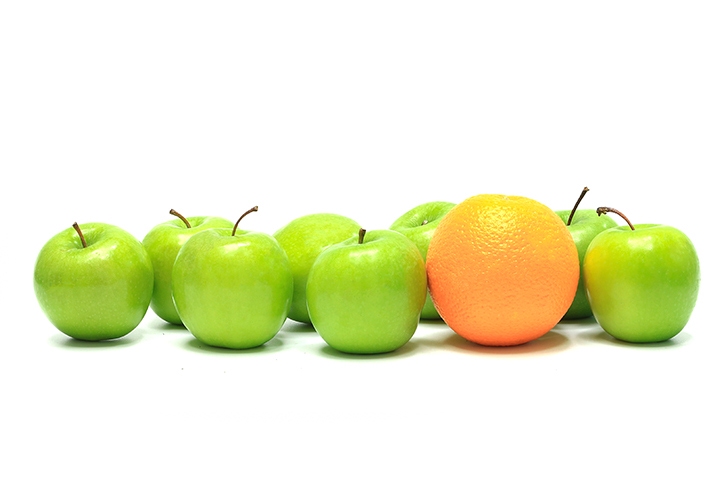 One orange in a group of green apples in front of a white background