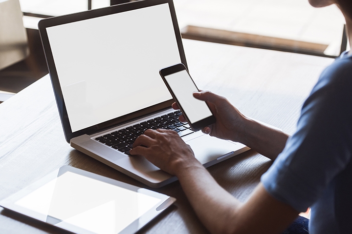 multitasking woman using tablet, laptop and smart phone, with blank screens, indoors on a table