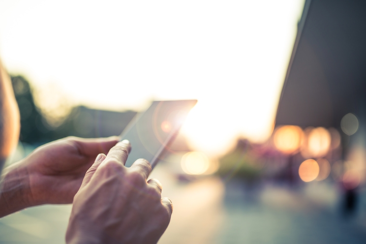 hand holding a mobile phone outside with the sunlight reflecting off of the screen