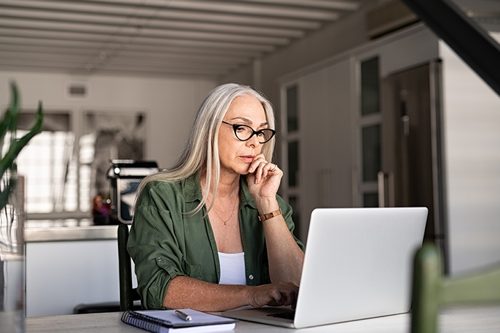 Focused old woman at home using laptop