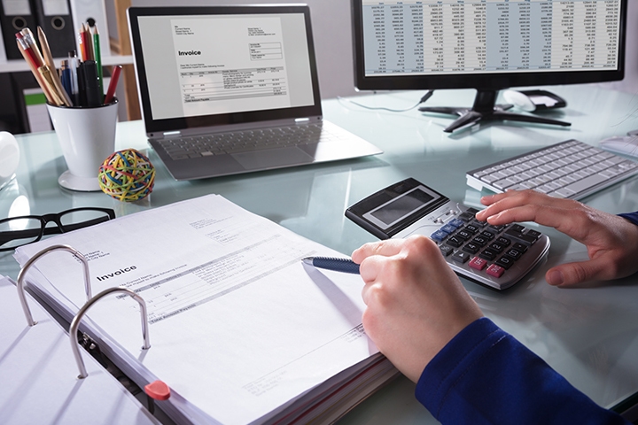 Homme d'affaires utilise un calculatrice et son ordinateur pour calculer les factures