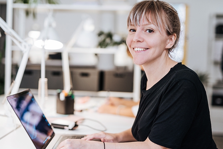 femme qui regarde le camera, en train de travailler sur son ordinateur