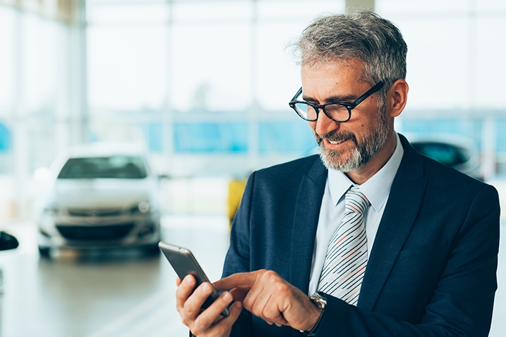 man in a business suit using his cellphone with a car in the background