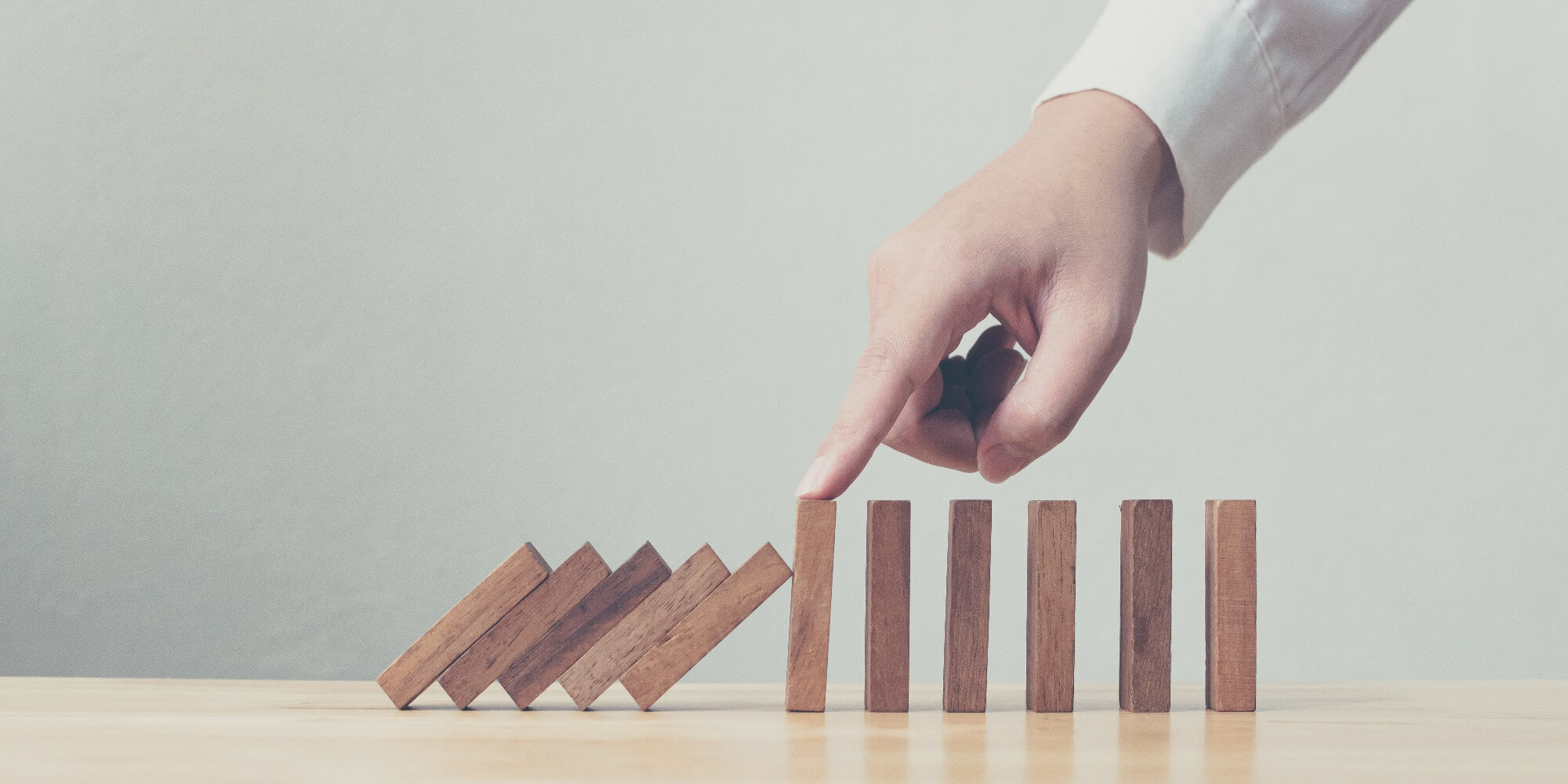 Dominoes falling down with a finger touching one of them