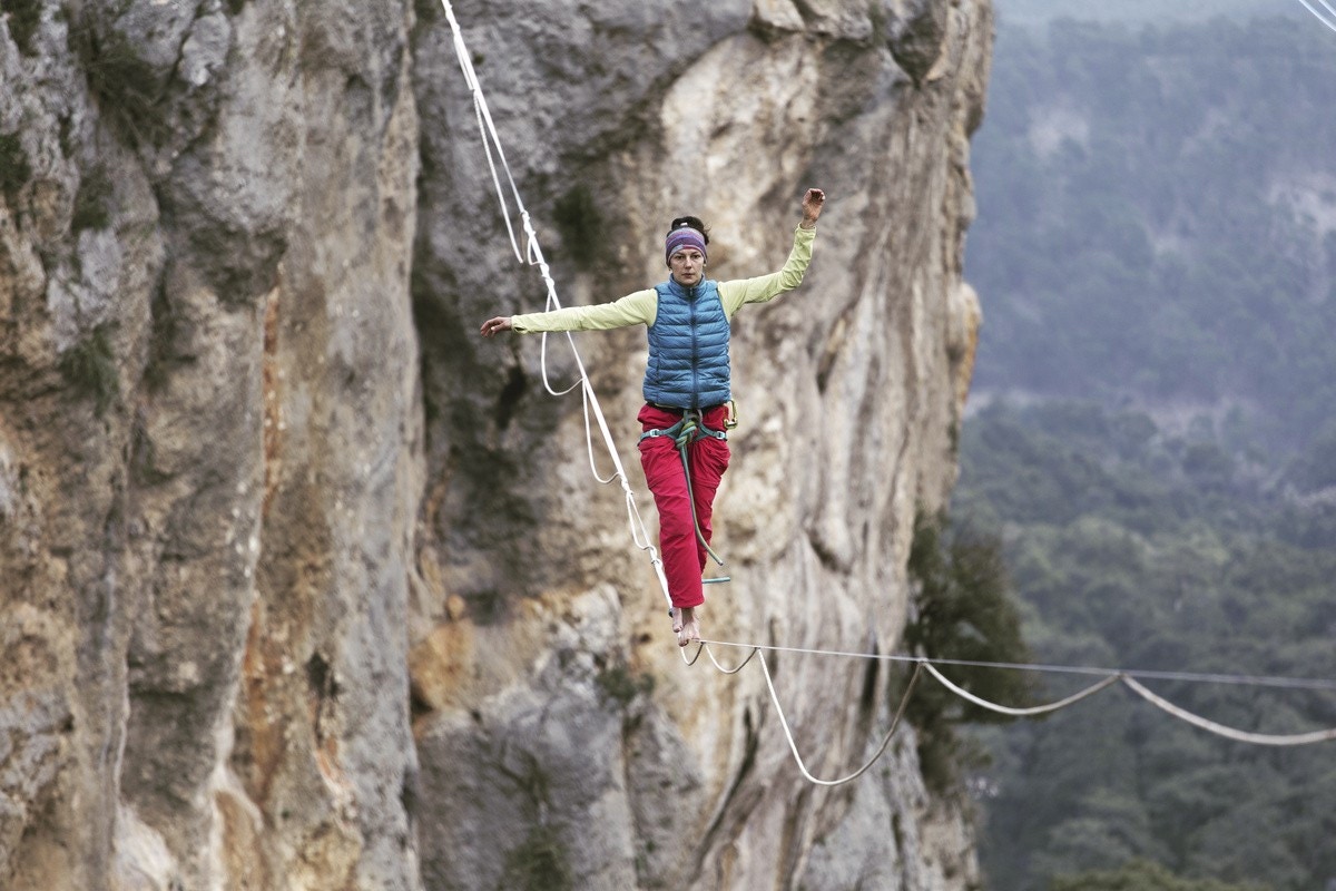 Adventurous woman tied to harness and walking along a tightrope