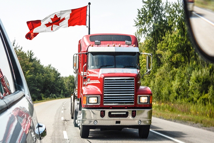 Tractor trailer driving down highway with Canadian flag flying