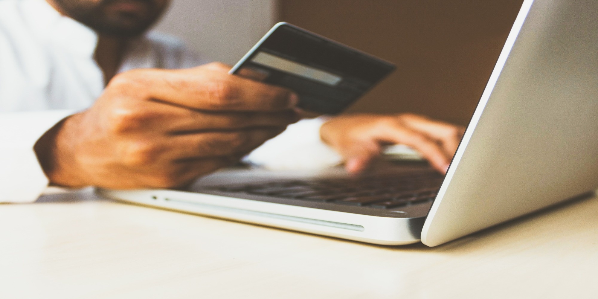 Person using laptop on desk holding credit card