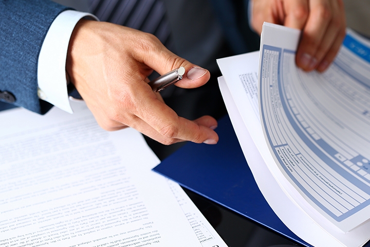 Male arm in suit offer insurance form clipped to pad and silver pen to sign closeup.
