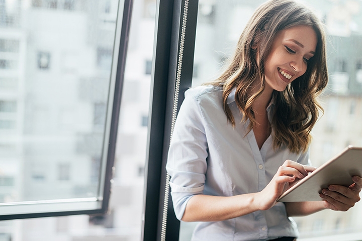 femme qui sourit et utilise son portable pres d'une fenetre