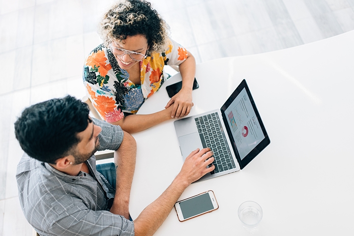 Two people sitting together working at white table with laptop