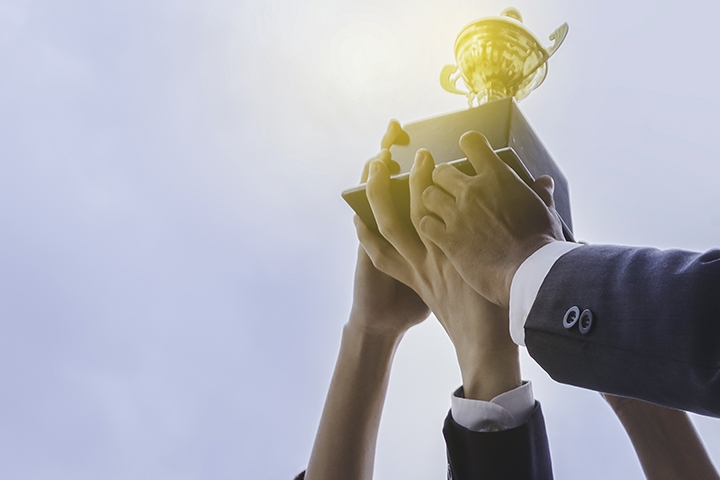 hands of business men and business women holding up a trophy