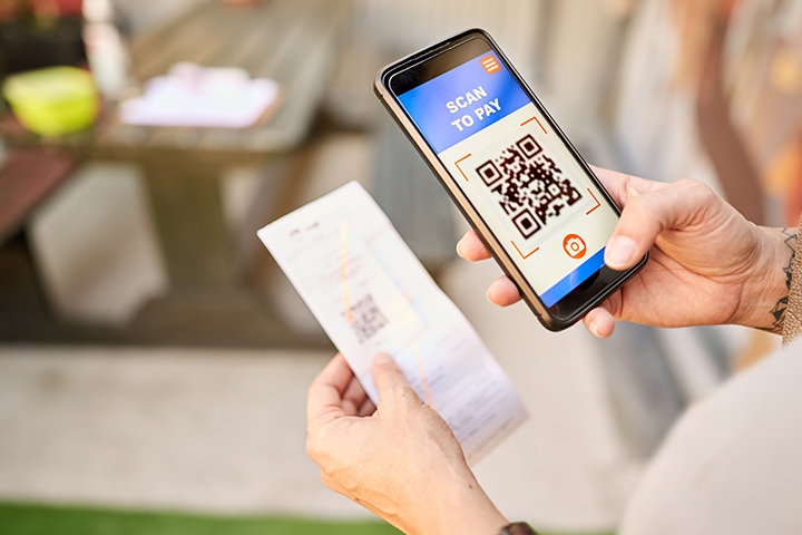 Shot of a person paying for a store purchase using her smartphone and a QR code on her receipt