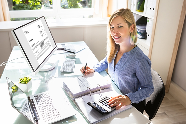 Businesswoman Calculating Bill With Computer And Laptop On Desk