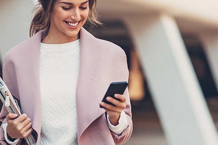 Business woman in lavender coat holding a mobile phone and a folder smiling