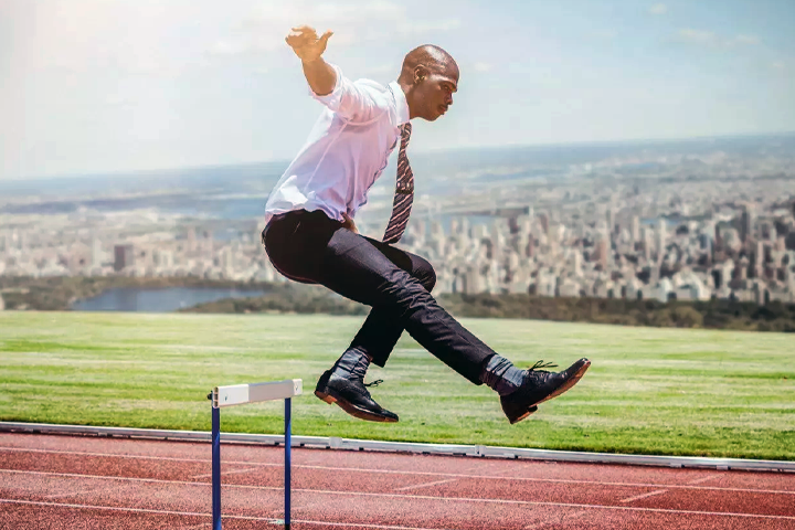 Businessman running and jumping over a hurdle on a track