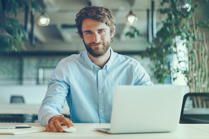 Business man working on laptop at desk smiling for camera