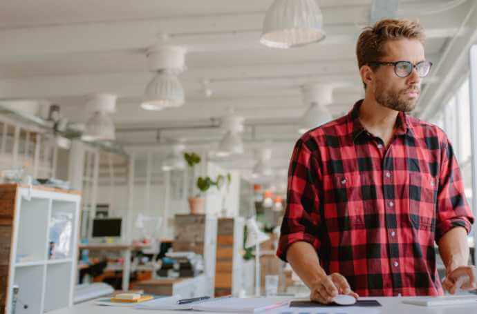 a man in a red and black checkred shirt and glasses on a standing desk in an office