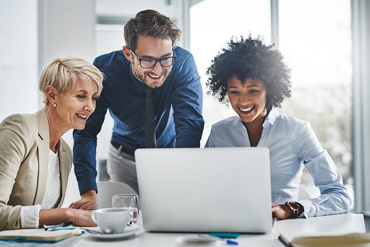 Diverse group of people smiling as they look at laptop