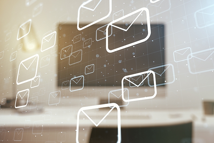 a monitor on a desk in a blurred background and abstract mail icons floating over it