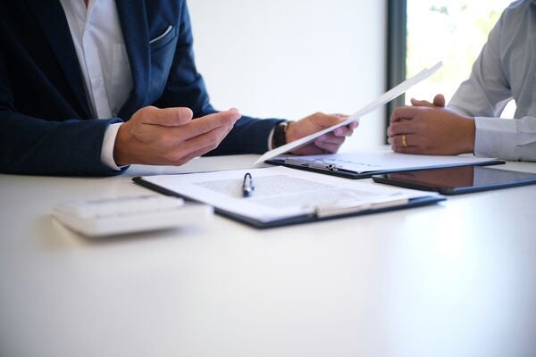 Two people sat a desk in an office talking over some documents and folders