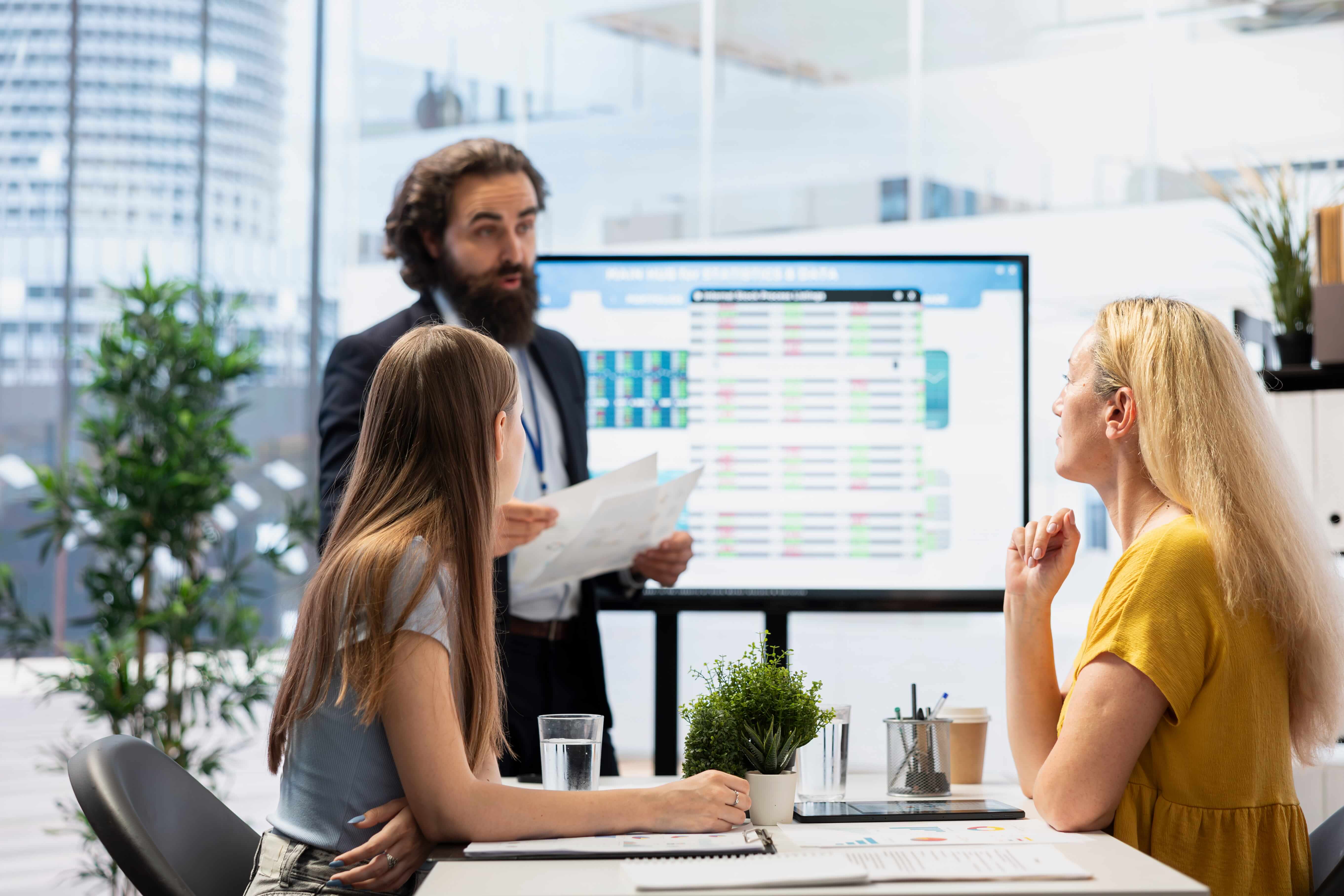 A group of colleagues in a modern office reviewing documents while another person presents a large display screen showing a detailed workflow or financial dashboard related to optimizing AP and AR processes.