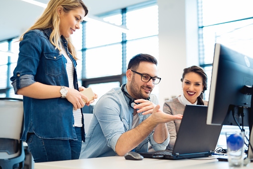 Three colleagues collaborating around a laptop in an office, reviewing digital content together during a team discussion.