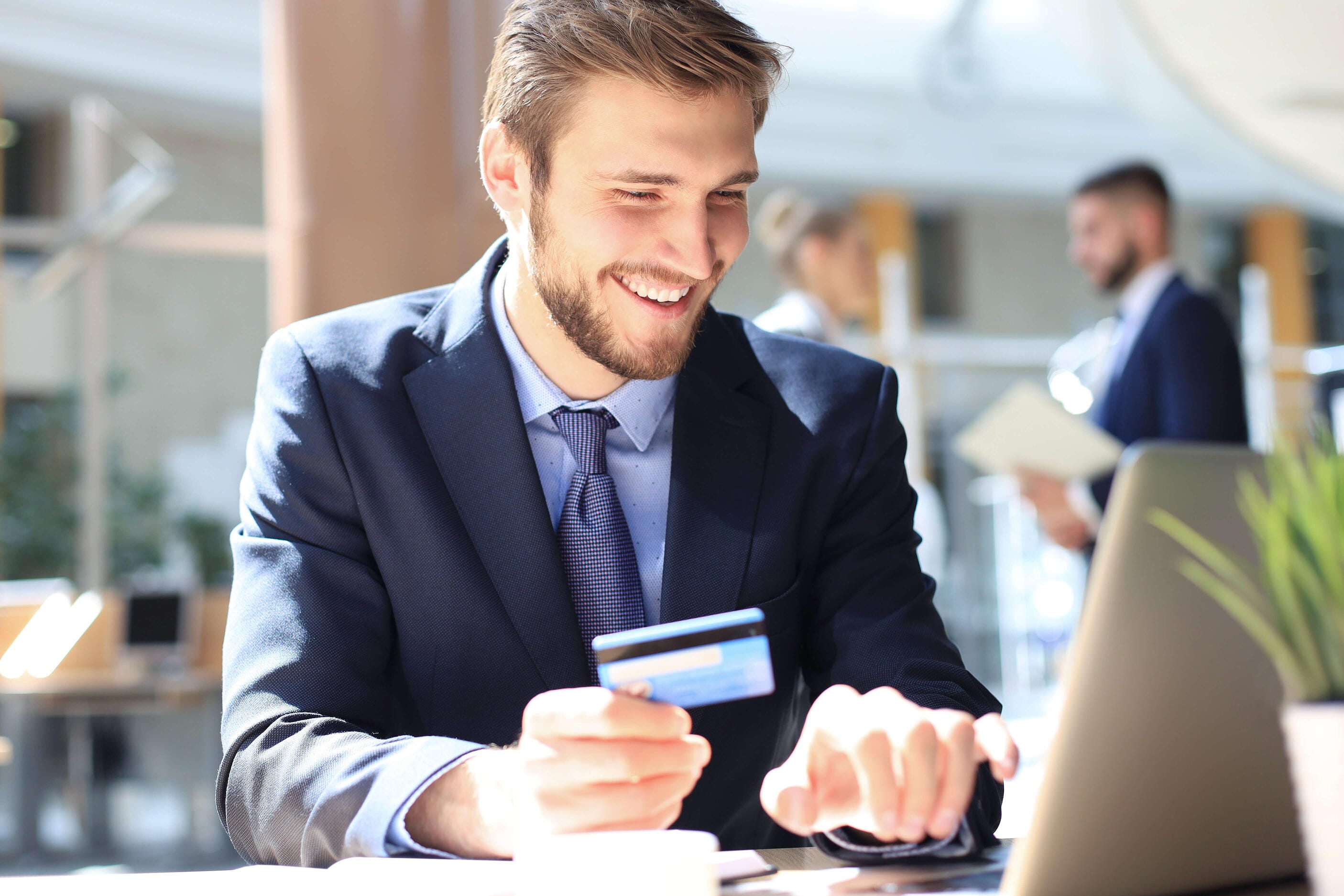 businessman holding a credit card and using a laptop smiling