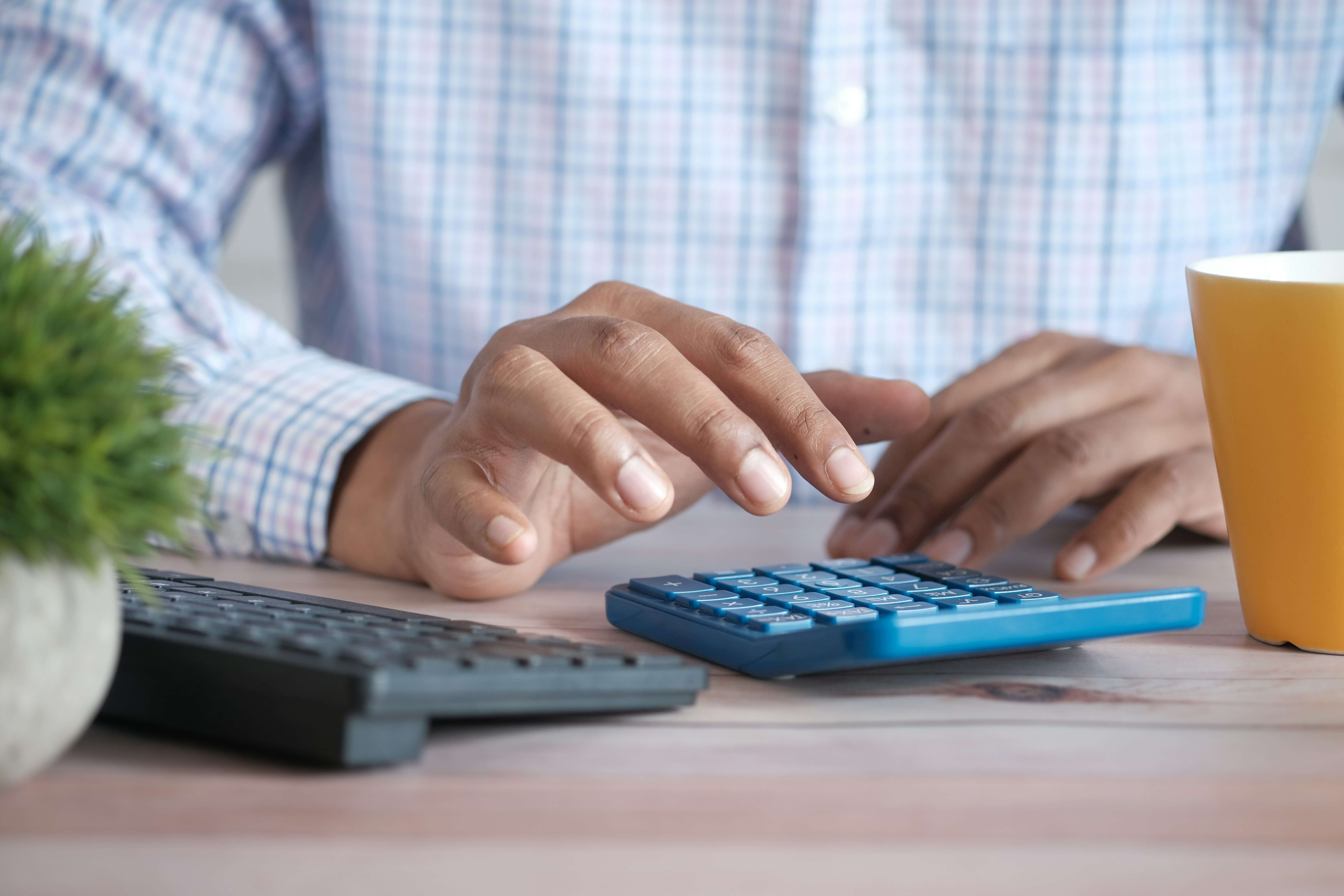 Close-up of a person using a calculator at a desk with a keyboard and a coffee mug, representing financial calculations and Accounts Payable workflows